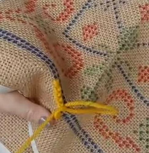 Hands stitching wool onto a jute canvas